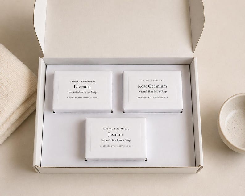 May include: A white gift box containing three rectangular bars of natural shea butter soap wrapped in white paper. Each label features the text Natural & Botanical, the scent name Lavender, Rose Geranium, or Jasmine, and Handmade with Essential Oils.