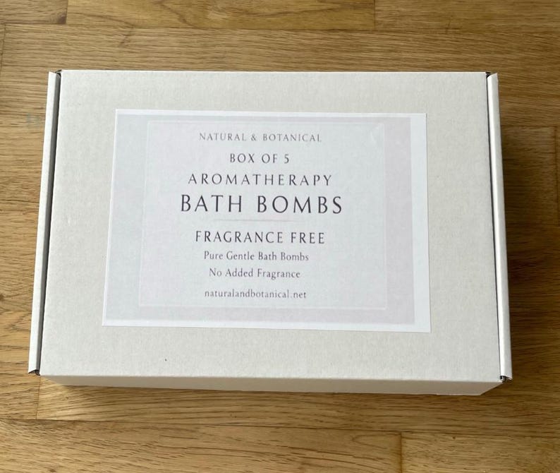 May include: A rectangular, off-white box with a label that reads "NATURAL & BOTANICAL BOX OF 5 AROMATHERAPY BATH BOMBS FRAGRANCE FREE." The label also states "Pure Gentle Bath Bombs" and "No Added Fragrance." The website naturalandbotanical.net is listed.