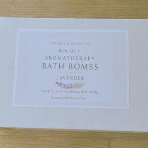 May include: A rectangular white box with a label that reads "NATURAL & BOTANICAL BOX OF 5 AROMATHERAPY BATH BOMBS LAVENDER." The label also includes the text "Handcrafted Aromatherapy Bath Bombs" and "naturalandbotanical.net."