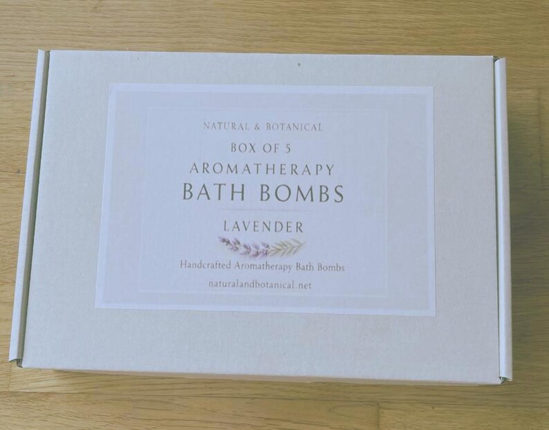 May include: A rectangular white box with a label that reads "NATURAL & BOTANICAL BOX OF 5 AROMATHERAPY BATH BOMBS LAVENDER." The label also includes the text "Handcrafted Aromatherapy Bath Bombs" and "naturalandbotanical.net."