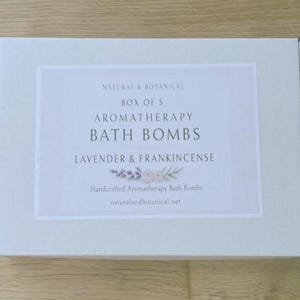 May include: A light gray box with a white label featuring the text "NATURAL & BOTANICAL BOX OF 5 AROMATHERAPY BATH BOMBS LAVENDER & FRANKINCENSE". The label also includes the text "Handcrafted Aromatherapy Bath Bombs" and a website address.