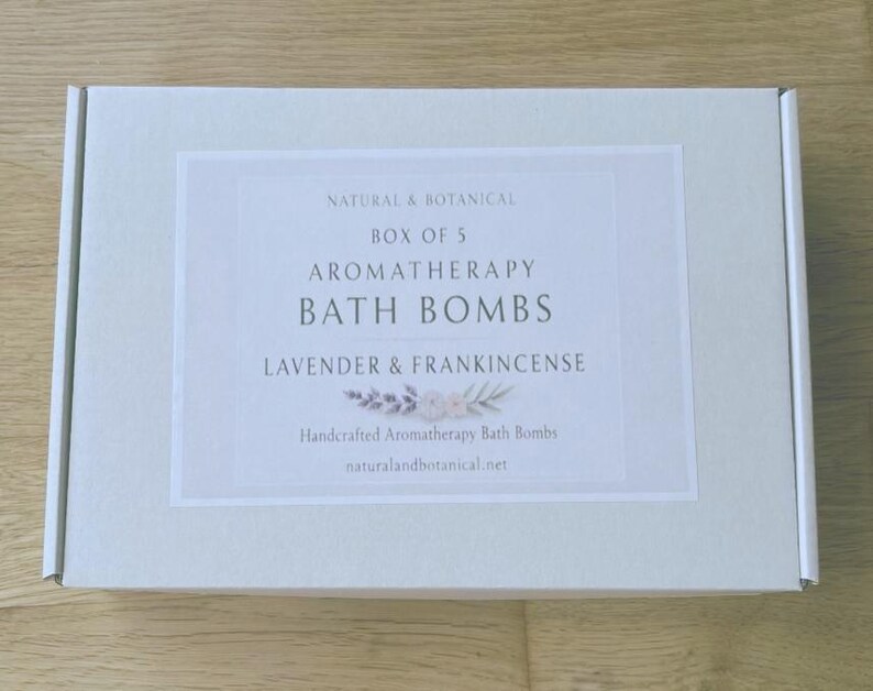 May include: A light gray box with a white label featuring the text "NATURAL & BOTANICAL BOX OF 5 AROMATHERAPY BATH BOMBS LAVENDER & FRANKINCENSE". The label also includes the text "Handcrafted Aromatherapy Bath Bombs" and a website address.