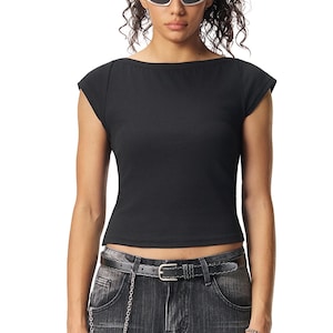 May include: Black cap-sleeve top with a boat neck. The fitted shirt is made of a solid black material. The model is wearing a pair of denim jeans with a black belt and silver chain.