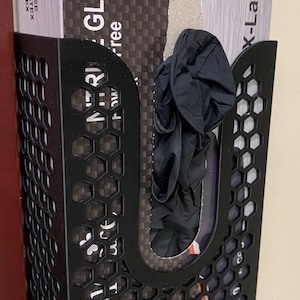 Op de afbeelding: Zwarte metalen handschoen dispenser met een honingraat ontwerp, met een doos met latexvrije handschoenen. De doos is gelabeld met "GLOVES" en "X-Large". Een paar zwarte handschoenen is zichtbaar in de dispenser.