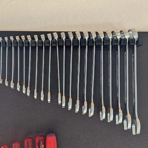 May include: A set of silver wrenches, ranging in size from small to large, are neatly organized on a black mounting board. The wrenches are arranged in a curved line, with each one clearly labeled with a number. The tools are designed for mechanical work.