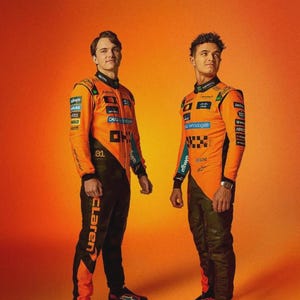 May include: Two people wearing orange and black racing suits. The suits have sponsor logos and the word "McLaren" on the pants. The background is a gradient of orange.