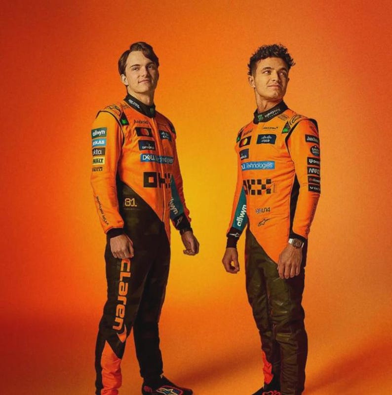 May include: Two people wearing orange and black racing suits. The suits have sponsor logos and the word "McLaren" on the pants. The background is a gradient of orange.