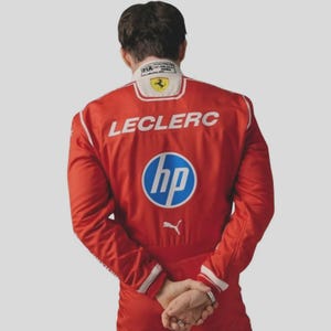 May include: A bright red racing suit featuring the name LECLERC in white lettering across the back. A large blue and white HP logo is centred below the name, with a white Puma logo underneath. The collar displays a Ferrari emblem and FIA text.