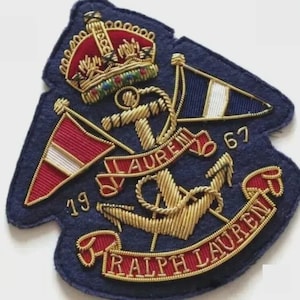 以下が含まれることがあります： 金色の錨、王冠、旗が刺繍されたネイビーブルーのパッチ。パッチには、赤いバナーで「LAUREN」と「RALPH LAUREN」の文字と、「19」と「67」の数字が含まれています。
