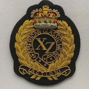 May include: Black embroidered patch with gold and multi-colored accents. The patch features a crown, laurel wreath, and text that reads "AMERICAN CLASSIC WEAR ACTION". The patch has a black border and is likely for apparel.