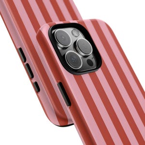 Op de afbeelding: Close-up van twee telefoonhoesjes met een verticaal gestreept patroon in roze en rood. De bovenste hoes heeft een zwarte cameralensbehuizing met meerdere lenzen.
