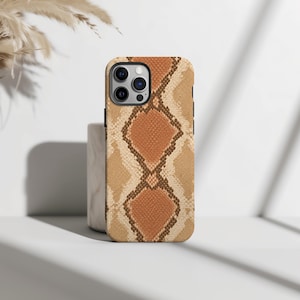 Könnte beinhalten: Eine Smartphone-Hülle mit einem sich wiederholenden rautenförmigen Muster in Beige-, Hellbraun- und Dunkelbrauntönen, das die Textur und das Aussehen von Schlangenhaut nachahmt. Die Hülle hat eine Aussparung für ein Dreifach-Kamerasystem.