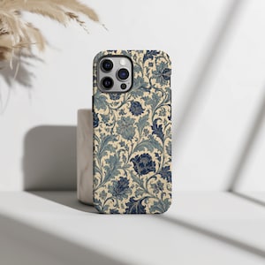 Op de afbeelding: Een smartphonehoesje met een gedetailleerd bloemenpatroon van donkerblauwe en gedempte blauwgroene bloesems, bladeren en krullende ranken op een crèmekleurige achtergrond. Het hoesje heeft een uitsparing voor een camera met drie lenzen.