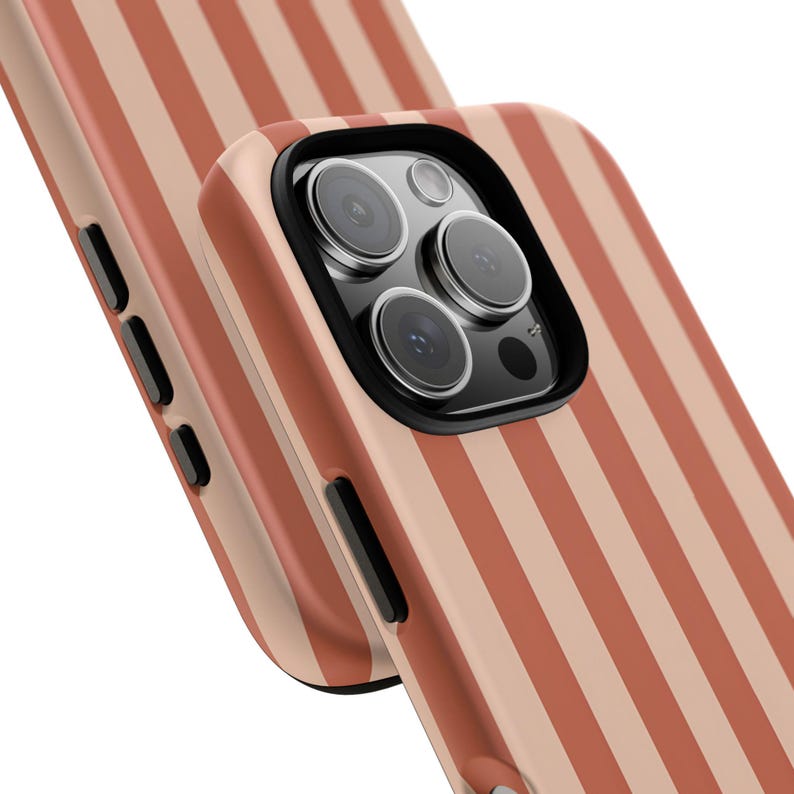 May include: Close-up of two phone cases with a repeating pattern of vertical stripes in shades of peach and cream. The phone case has a black camera lens protector.