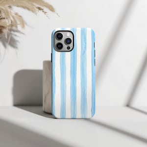Könnte beinhalten: Eine Smartphone-Hülle mit einem vertikalen Streifenmuster in Hellblau und Weiß. Das Design hat eine weiche, aquarellartige Textur mit variierender Farbintensität über die Streifen hinweg. Die Hülle enthält einen Ausschnitt für ein Dreifach-Kamerasystem.