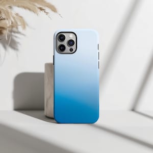 Könnte beinhalten: Eine Smartphone-Hülle mit einem glatten Farbverlauf, der von einem hellen, blassen Blau an der Oberseite zu einem tiefen, kräftigen Blau an der Unterseite übergeht. Die Hülle hat einen rechteckigen Ausschnitt für eine Dreifachkamera auf der Rückseite.