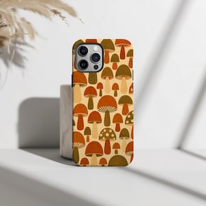 Könnte beinhalten: Eine Handyhülle mit einem wiederkehrenden Muster aus verschiedenen Pilzen in Orange-, Braun- und Cremetönen. Das Design zeigt unterschiedliche Pilzformen, einige mit gepunkteten Kappen, auf einem hellen cremefarbenen Hintergrund.
