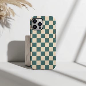 Op de afbeelding: Een smartphonehoesje met een herhalend dambordpatroon in afwisselende tinten van gedempt blauwgroen en crème. Het hoesje heeft een nauwkeurige uitsparing voor de cameramodule aan de achterzijde, voorzien van drie ronde lenzen en een flitser.