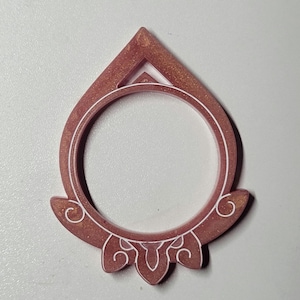Op de afbeelding: Een decoratieve, druppelvormige hars hanger in een stoffige roze kleur met gouden spikkels. De hanger heeft een cirkelvormige opening en witte decoratieve accenten. De bovenkant van de hanger heeft een driehoekige vorm.