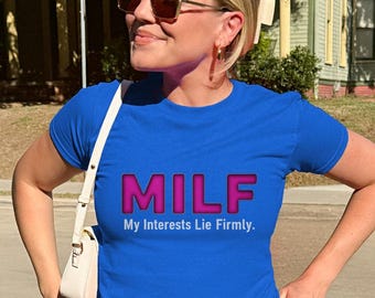 May include: A blue t-shirt with the word "MILF" in pink and the text "My Interests Lie Firmly." The shirt is paired with light-wash jeans. The person is wearing sunglasses and a white purse.