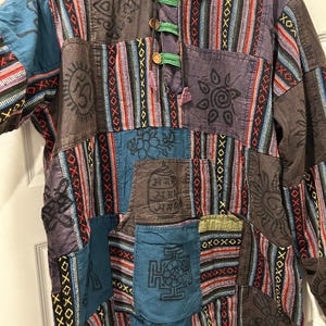 May include: A patchwork jacket with a variety of colors and patterns. The jacket features a mix of blue, brown, purple, and red fabrics with geometric and floral designs. It has a mandarin collar, wooden buttons, and a hood.