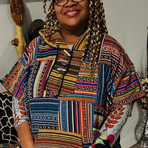 May include: A colorful patchwork poncho with a hood and pockets. The poncho features a variety of patterns and colors, including stripes, geometric shapes, and fringe at the bottom. The sleeves are long and patterned, and the poncho is worn by a person.