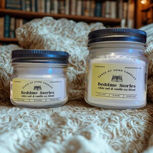 May include: Two glass jar candles with black lids. The labels read "Bedtime Stories" and "white oak & vanilla soy blend." The background includes a bookshelf and a textured blanket. The candles are handmade.