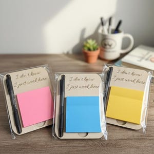 Puede incluir: Tres juegos de notas adhesivas con bolígrafos. Cada juego incluye un bloc de notas adhesivas rosas, azules o amarillas, un bolígrafo negro y un respaldo de cartón con el texto "I don't know, I just work here."