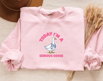 Op de afbeelding: Een lichtroze sweatshirt met de tekst "TODAY I'M A" boven een cartoon gans met een stethoscoop, en de woorden "SERIOUS GOOSE" eronder. De sweatshirt is gemaakt van een zacht materiaal.