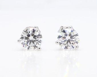 May include: A pair of diamond stud earrings. Each earring has a large, round, brilliant-cut diamond set in a silver or white gold prong setting. The diamonds are clear and reflect light, creating a brilliant sparkle.