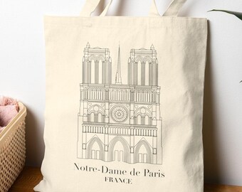 May include: Cream-colored tote bag featuring a black line drawing of Notre-Dame de Paris. The text "Notre-Dame de Paris FRANCE" is printed below the illustration. The bag has long handles and is made of a natural fabric.
