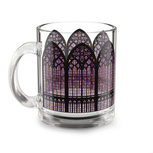 May include: Clear glass coffee mug featuring a colorful stained-glass window design. The design includes shades of purple, blue, yellow, and red, with black outlines. The mug has a curved handle and a transparent appearance.