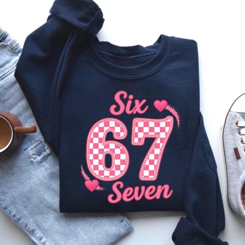 May include: Navy blue sweatshirt with the words "Six 67 Seven" in pink. The number "67" is in a pink and white checkered pattern. Two pink hearts are on the design.