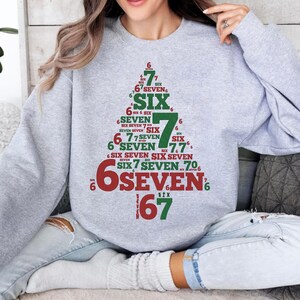 May include: A light gray sweatshirt featuring a Christmas tree design made of the numbers and words "six" and "seven" in red and green. The sweatshirt is a comfortable, casual style.
