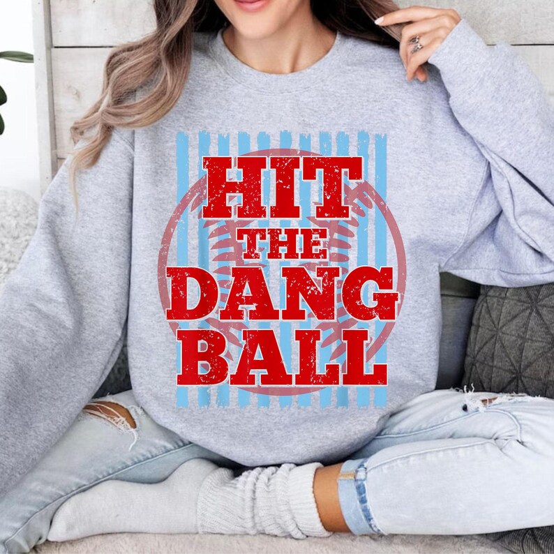 May include: A light gray sweatshirt with the text "HIT THE DANG BALL" in red, inside a red circle with blue stripes. The sweatshirt is a crew neck style.