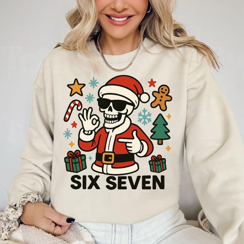 May include: Beige sweatshirt with a Christmas-themed graphic. The design features a skeleton wearing a Santa hat and sunglasses, surrounded by festive elements like a candy cane, gingerbread man, and presents. The text "SIX SEVEN" is printed below the graphic.