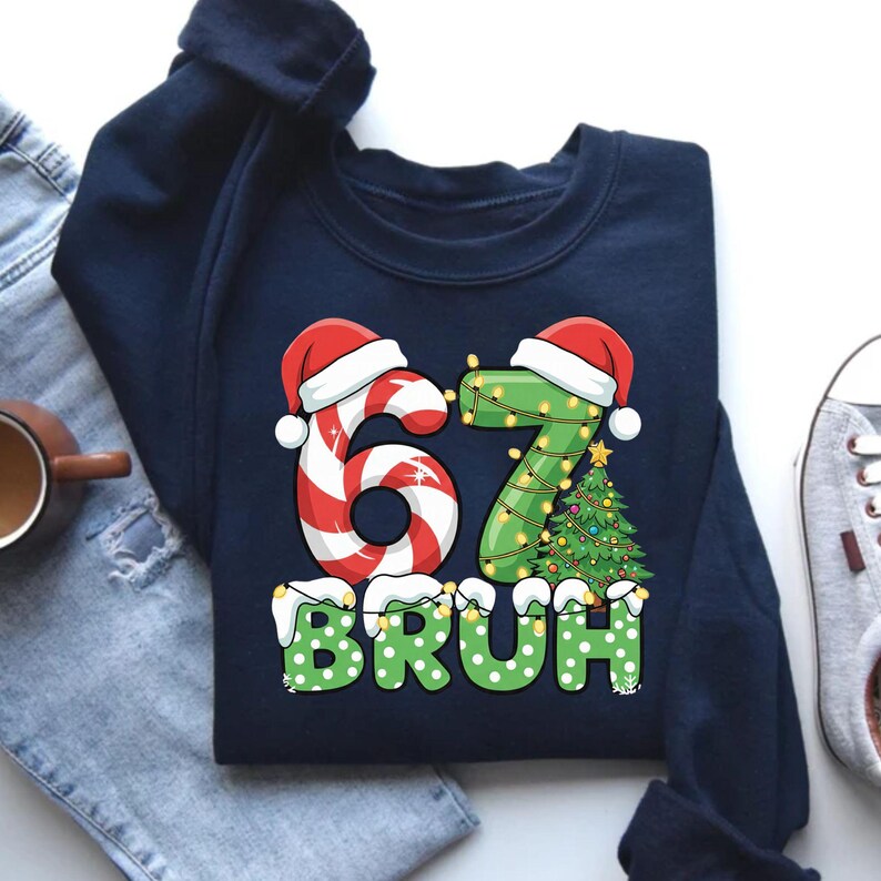 May include: Navy blue sweatshirt with a festive Christmas design. The graphic features the numbers "67" decorated with candy cane and Christmas lights, topped with Santa hats. The word "BRUH" is in green with white polka dots.