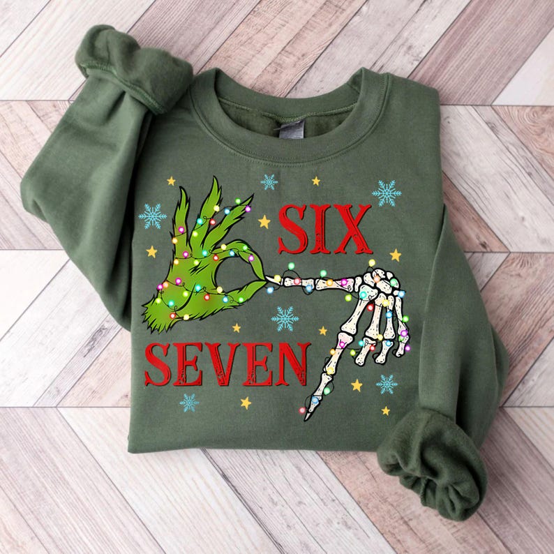 May include: Green sweatshirt with a graphic design featuring a green hand making an "okay" sign with a skeleton hand. The words "SIX" and "SEVEN" are in red, with snowflakes and stars.