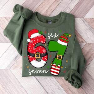 May include: Green sweatshirt with a festive Christmas design. The number 6 is red with a Santa hat and belt, the number 7 is green with an elf hat and striped socks. The word "six" and "seven" are written in white.