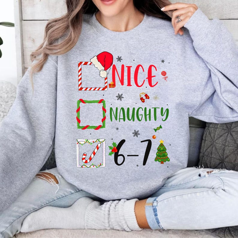 May include: A light gray sweatshirt with a Christmas-themed graphic. The graphic includes the words "NICE" and "NAUGHTY" with check boxes and festive decorations. The number "6-7" is also displayed.