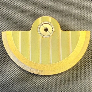 May include: A gold-colored, semi-circular mechanical component with a central circular bearing. The component has a fan-like design with vertical striped detailing and a textured surface. The overall shape is reminiscent of a stylized fan or gear.
