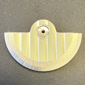 May include: A fan-shaped, metallic object with a central circular component and a series of vertical stripes. The object has a gold and silver color scheme, with a brushed metal finish on the edges. The design is symmetrical and appears to be a mechanical part.