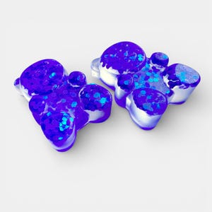 May include: Two abstract, purple resin objects with a cluster of rounded shapes. The resin is filled with blue glitter, and the objects have a white base. The shapes are reminiscent of a flower or a cluster of bubbles.