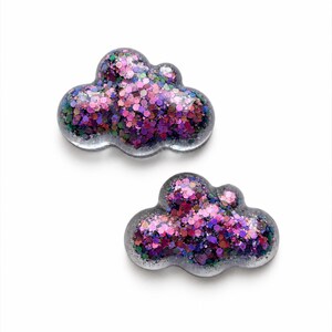 May include: Two cloud-shaped ornaments made of clear resin filled with a dense mixture of chunky pink, purple, blue, and green glitter. The shapes have rounded edges and a smooth, glossy finish, showcasing the reflective, multi-colored sparkles.