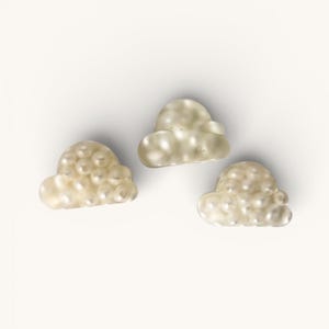 May include: Three cloud-shaped decorative objects. Each cloud is a creamy, pearlescent color, with a bubbly texture. The clouds are arranged on a white background. The objects appear to be made of glass or a similar material.
