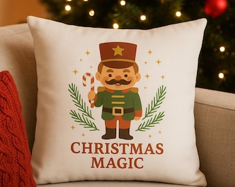 May include: A cream-colored square pillow featuring a cartoon nutcracker soldier with a candy cane and the words "CHRISTMAS MAGIC" in brown. The soldier wears a green uniform, brown hat, and black boots. Gold stars and green sprigs surround the soldier.