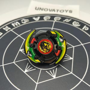 May include: A black, green, and yellow spinning top toy with a red center featuring a dragon graphic. The toy has a circular design with a series of blades and is set on a black surface with a white geometric pattern. The text "UNOVATOYS" is visible in the background.