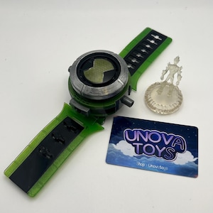 May include: A green and black toy watch with a silver bezel and a black band. A small, clear plastic figure stands on a circular base. A card with the text "UNOVA TOYS" is also present.