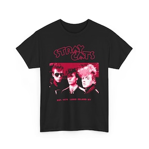 Op de afbeelding: Zwart t-shirt met een rood-witte afbeelding van de band Stray Cats. De afbeelding bevat de naam van de band en een gestileerde afbeelding van de bandleden. De tekst "EST. 1979 LONG ISLAND NY" is ook aanwezig.