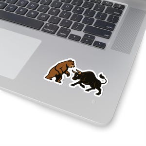 May include: A sticker featuring a brown bear and a black bull in a stylized illustration. The bear is on the left, and the bull is on the right, with both animals facing each other. The sticker is on a laptop.